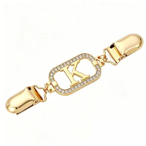 Close-up detail of gold-tone metal clothing clip featuring a rhinestone-paved letter K element.