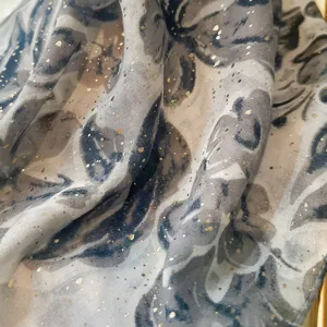 Close-up detail of grey floral linen scarf, delicate gold glitter pattern, soft draped texture.