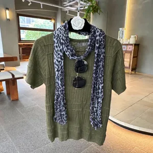 Detail view of olive green knit short-sleeve top with leopard scarf and sunglasses display.