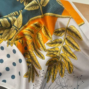Close-up detail of silk scarf featuring botanical leaf print and geometric polka dot design.