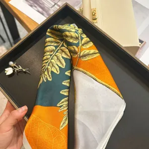 Silk square scarf detail, vibrant botanical fern leaf print in orange and green, silky.