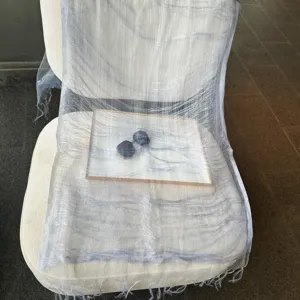 Detailansicht des durchsichtigen, kühlen grauen Seidenschals, der elegant über dem Stuhl liegt.
