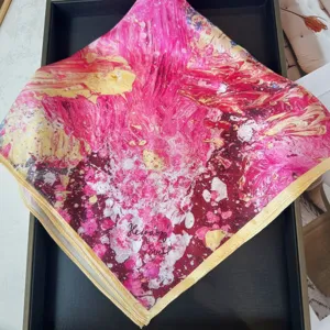 Close-up detail of the pink and gold abstract printed silk square scarf with fine rolled edges.