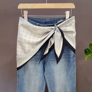 Detail view of a black and white paisley triangle silk scarf styled on denim waistband.