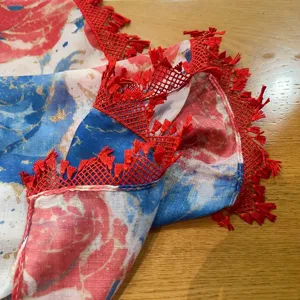 Detailansicht eines leichten Blumenschals mit rotem Spitzenbesatz und feinen Fransen.
