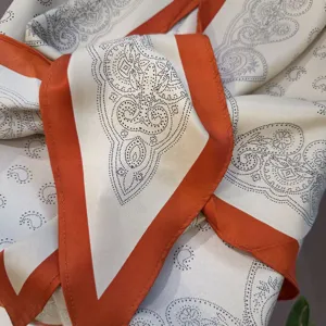 Silk scarf detail view, elegant paisley print with bold orange border, chic neckerchief.