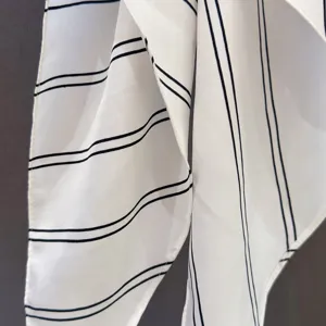 Close-up detail view of white fabric triangle scarf featuring elegant black double stripe pattern.