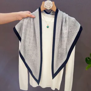 Detailed view of grey paisley printed square silk scarf draped on white knit sweater.