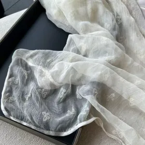 Delicate sheer bow pattern detail close-up of lightweight sunscreen scarf, elegant ivory fabric.