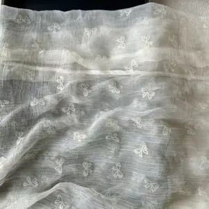 Close-up detail of sheer white women scarf featuring delicate crinkled texture and cute bows.