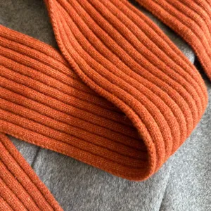 Orange ribbed knit scarf detail close up, soft cozy texture, fashionable winter neck accessory.