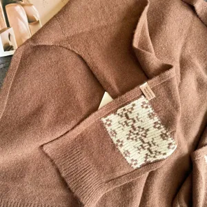Close-up detail of brown wool knit shawl scarf featuring jacquard patch and brand label.