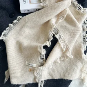 Cozy beige knitted scarf with chic frayed lace edges and delicate pendant detail, winter warm.