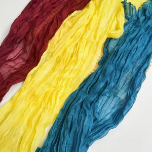 Detailed view of crinkled gauze scarves in vibrant burgundy, yellow, and blue colors.