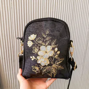 Detailed view of black embroidered crossbody bag with gold floral patterns and metal hardware.