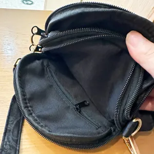 Detail shot of a black round multi-zipper crossbody bag showing inner pocket structure.