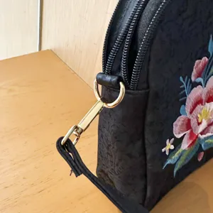 Detailed view of black Chinese style floral embroidered shell bag with gold hardware.