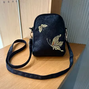 Black fabric crossbody bag with gold embroidered butterfly pattern, stylish ethnic design.