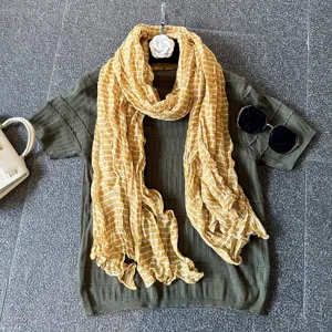 Detailed view of a yellow striped crinkle scarf paired with an olive green knit top, chic style.