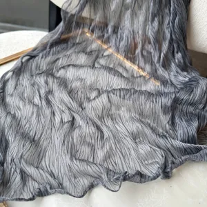 Close-up detail of the dark grey pleated textured long scarf, showing its pearlescent sheen.