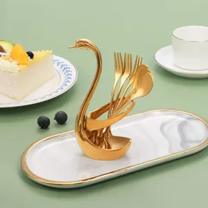 Gold swan cutlery holder set with stainless steel dessert forks and spoons on a ceramic tray.