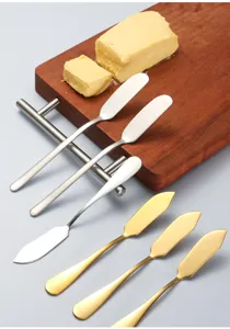 Detail shot of stainless steel butter knives and golden spreading tools on wooden cutting board.