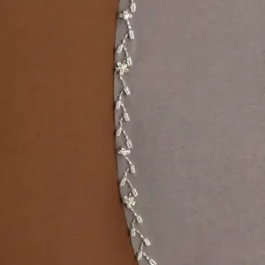 Bridal veil detail shot featuring delicate handmade beaded floral lace trim, wedding accessory.