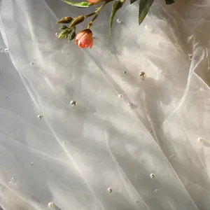 Gedetailleerd overzicht van witte tule bruidssluier versierd met parels en roze bloem.