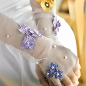 Nahaufnahme von eleganten Braut-Netzarmstäumern mit zarten 3D lila Blumen und Perlen.