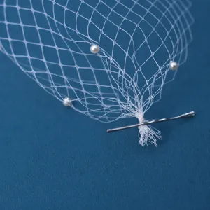 Dettaglio della clip per capelli in velo di rete bianco con perle per servizi fotografici.