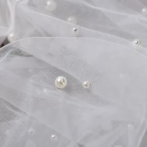 Detailopname van witte tule stof gedecoreerd met elegante parels en kleine metalen studs.