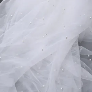White tulle fabric detail featuring delicate pearls, soft wedding veil mesh material.