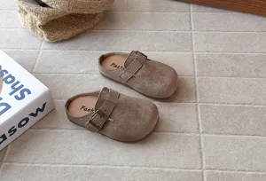 Detailed view of brown suede slip-on kids mules featuring adjustable buckle strap and soft sole.