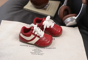 Close-up detail of retro red kids casual sneakers with white laces and stylish side stripes.