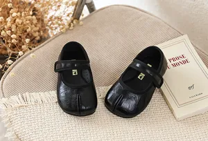 Close-up detail van zwarte split-toe lederen mary jane schoenen op stoel met boekdecor.