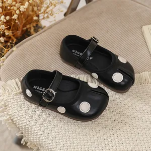 Detailopname van zwarte Mary Jane schoenen met gespleten teen en witte stippen voor kinderen.