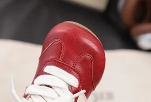 Kids casual retro sports sneakers detail view featuring red leather upper and white laces.