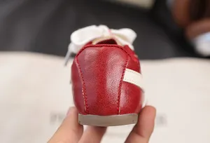 Red retro kids sneakers heel detail, casual footwear with white side stripes and laces.