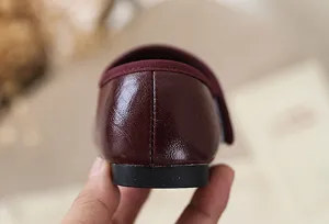 Gedetailleerd overzicht van bordeauxlederen kinderschoen met zachte zool en nette stiksels op hiel.