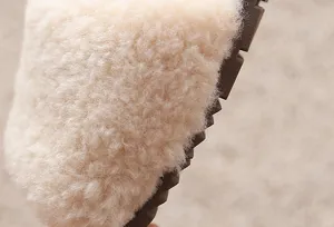 Gros plan de pantoufles en peluche duveteuse avec dessus polaire beige et semelle marron.