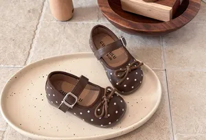 Detail shot of brown kids polka dot Mary Jane shoes with bow decoration on ceramic tray.