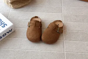 Detailed close-up of children's brown suede slip-on clogs featuring an adjustable side buckle and soft sole.