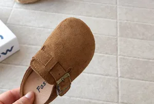 Close-up detail of brown suede children clog shoe with metal buckle and soft sole.