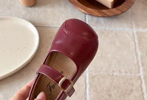 Close-up detail of burgundy kids mary jane shoe with metallic buckle and soft leather.