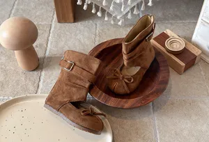 Close-up detail shot of brown suede toddler boots featuring cutout design, chic bow and metal buckle.