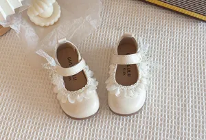 Dettaglio in primo piano di scarpe in pelle per bambine crema con volant in pizzo e perle.