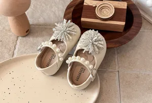 Detail shot of girls beige leather shoes, crystal flower embellishment, pearl strap design.