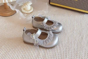 Dettaglio scarpe Mary Jane metallizzate da bambina, pelle argentata con volant in pizzo.