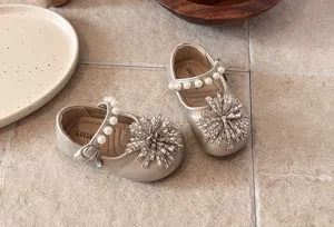 Close-up of toddler gold princess shoes featuring pearl straps and sparkling rhinestone flower details.
