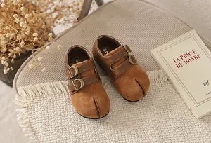 Zapatos de cuero marrón vintage para niños con punta dividida y hebillas metálicas dobles.